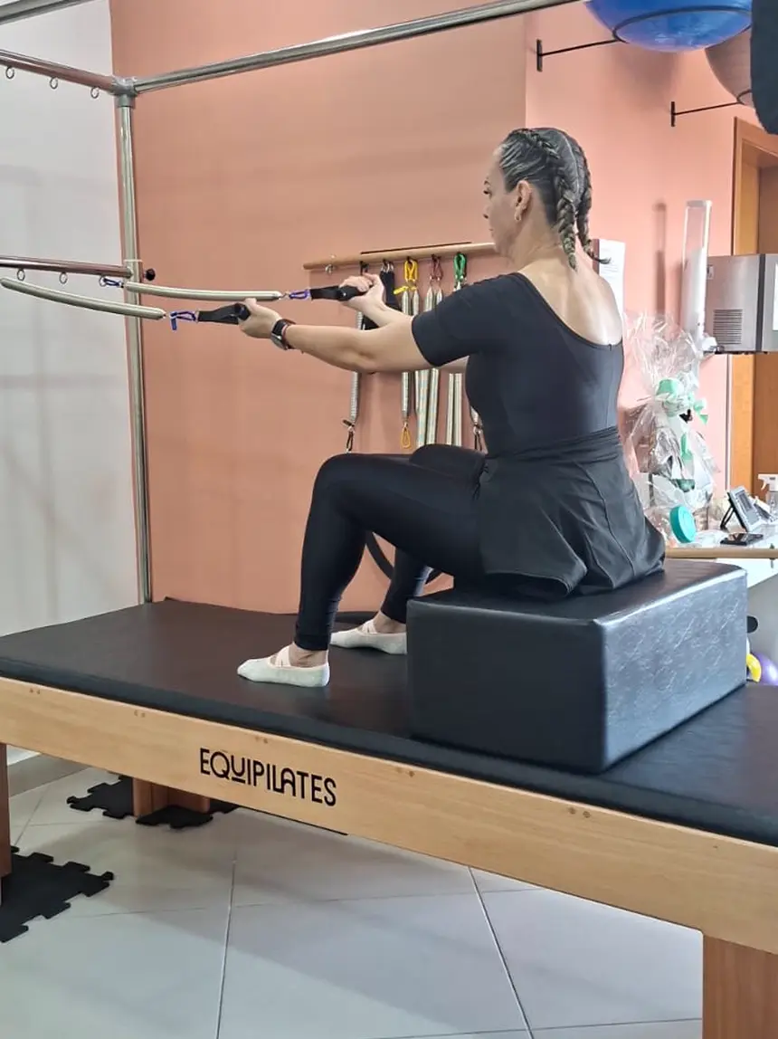 Aluna executando exercício de braços no Cadillac, diante da parede goiaba do studio